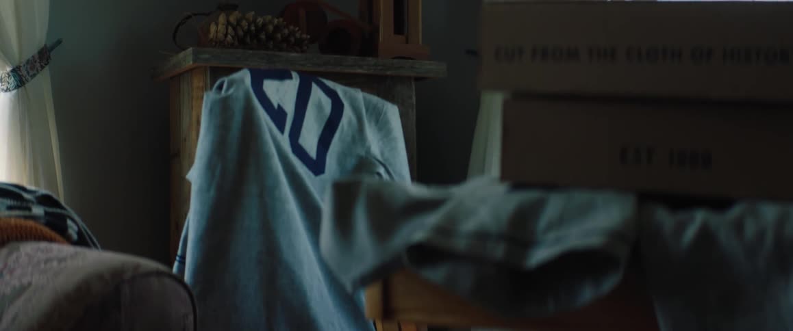 A numbered sports jersey is on the back of a chair in a bedroom near boxes