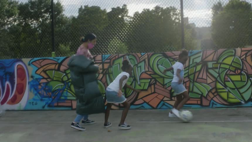 A woman is in a park playing soccer with two young girls