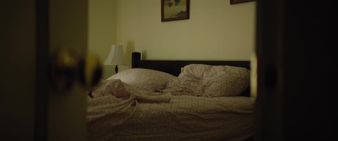 A bedroom door is open revealing an unmade bed
