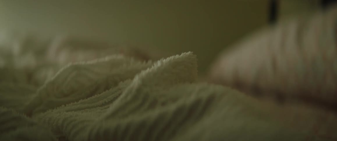 Rumpled bedspread on unmade bed sits a distance from pillow
