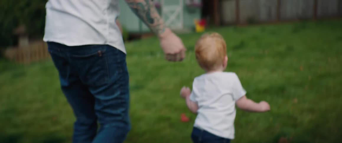 A man rubs his young sons head before he runs across the yard playing