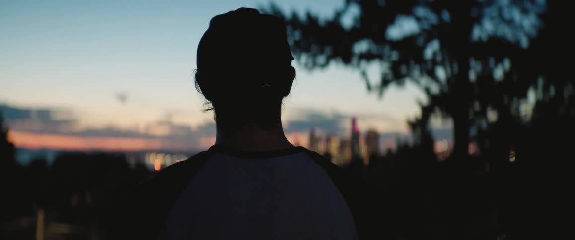 The silhouette of a person in cap and jersey tossing a baseball up and catching it
