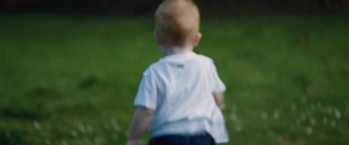 A boy runs around his backyard throwing a ball