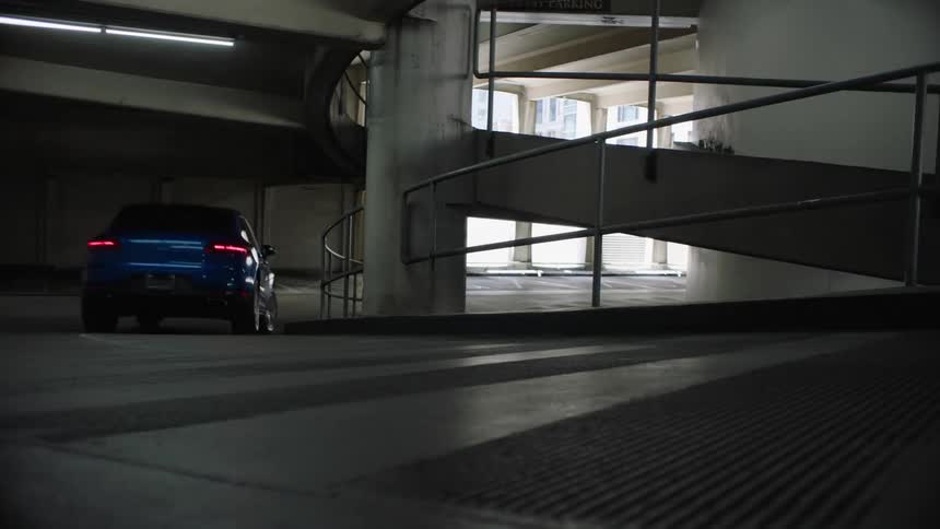 A car drives down a ramp and pulls out of a parking garage