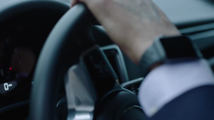 Man with suit and space gray watch uses steering wheel of sports car