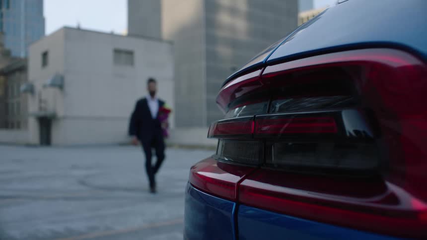 A man clicks his car alarm as he walks toward his vehicle carrying a backpack and bouquet
