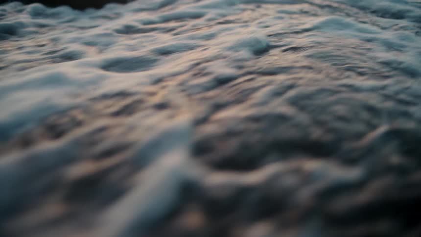 Water washes over a stone on a beach in the evening