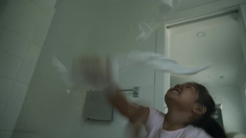 A little girl is in a bathroom laughing as she throws toilet paper into air and plays with it