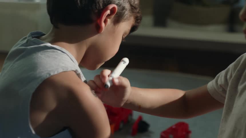 Boys sit on floor coloring on each other with a marker