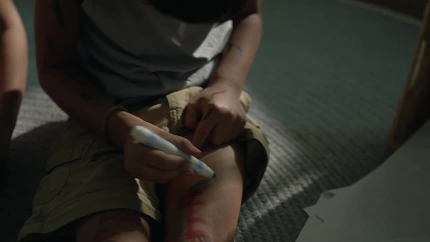Two children draw on their legs with markers