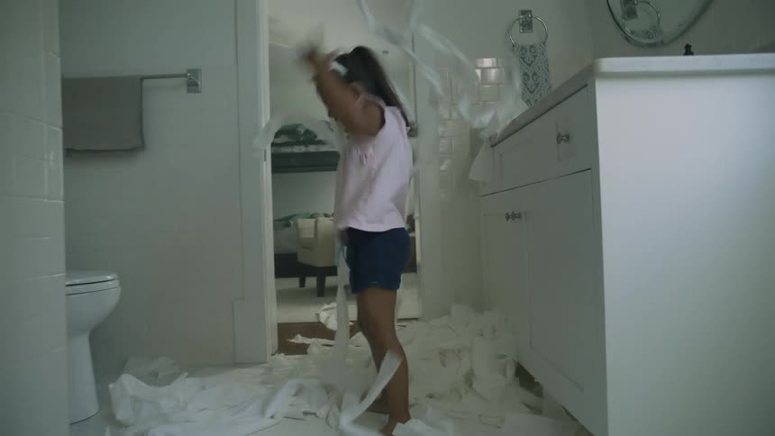 A little girl is in a bathroom laughing as she throws toilet paper into air and plays with it