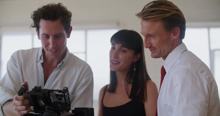 Filmmaker shows footage to a couple of actors while laughing inside a white room