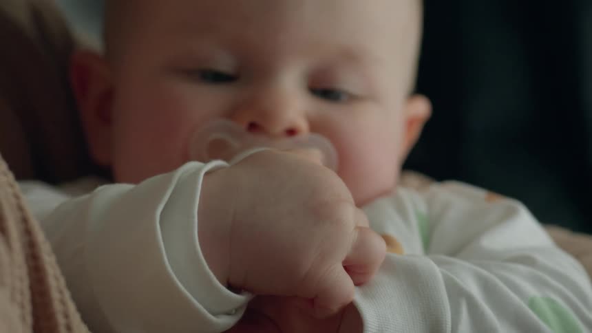 A baby plays with his own hands and fingers while being cradled