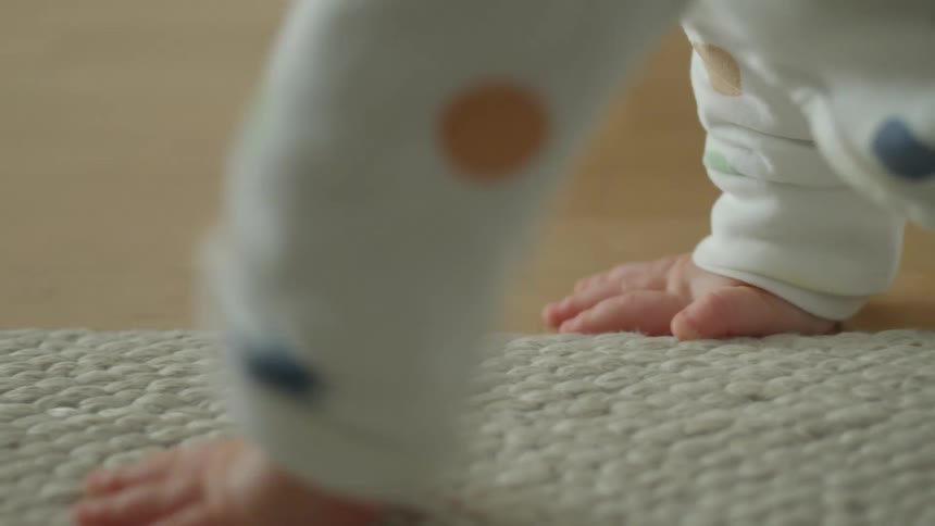 A small infant slowly plants its hand on the floor as it crawls through a room