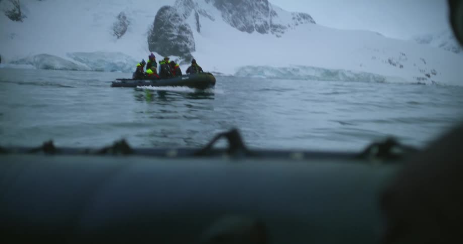 People on a raft in the ocean in front of a snow covered mountain