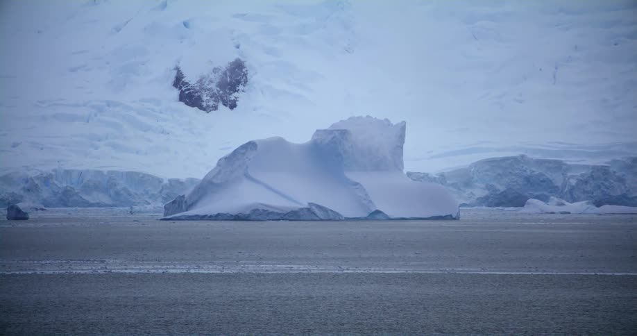 Iceberg floating over the surface of the ocean next to a mountain in the arctic