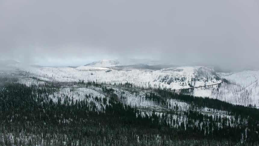 Clouds move over snow covered forested mountains