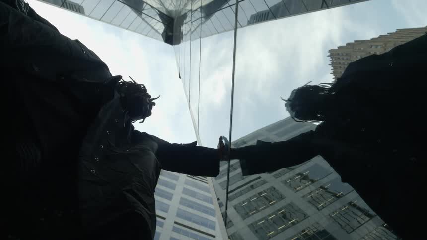 A man puts his hand on the glass facade of a building touching his reflection