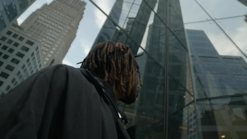 A man stands looking at the city buildings reflected in the glass facade