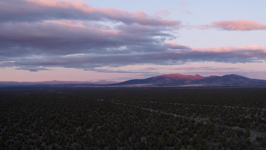 Clouds and mountain peak tinged pink with sunrise over flat lands covered with brush
