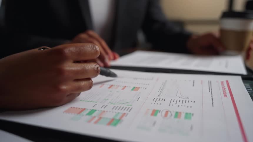 A pair of coworkers in an office examine printed reports together at a table