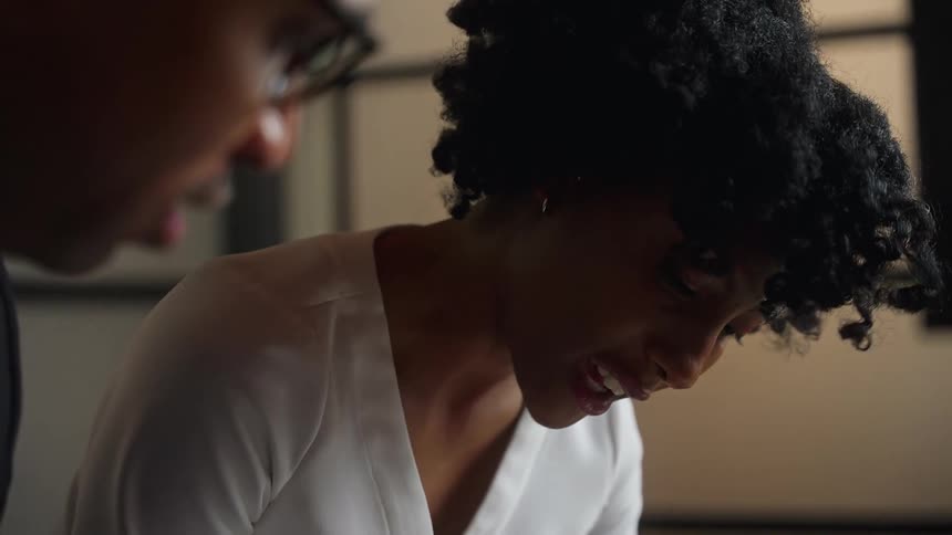 A man and a woman in an office talk as they look down at something