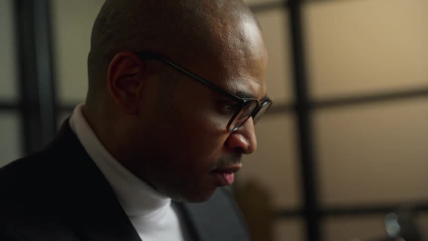 A man in an office puts his glasses on as he concentrates