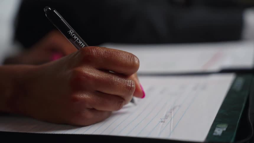 A woman sits in an office next to a man and writes in a notebook
