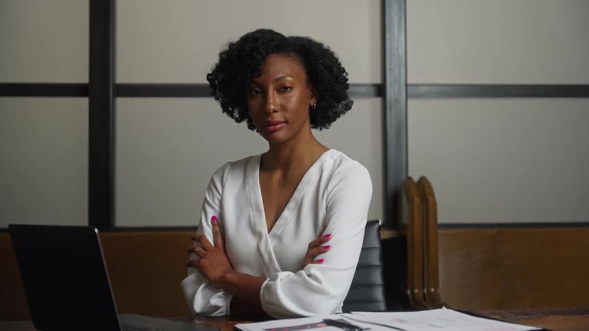 A woman sitting in an office meeting room folds her arms while looking confident