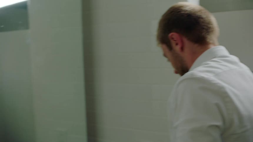 A man is washing his face in a public bathroom