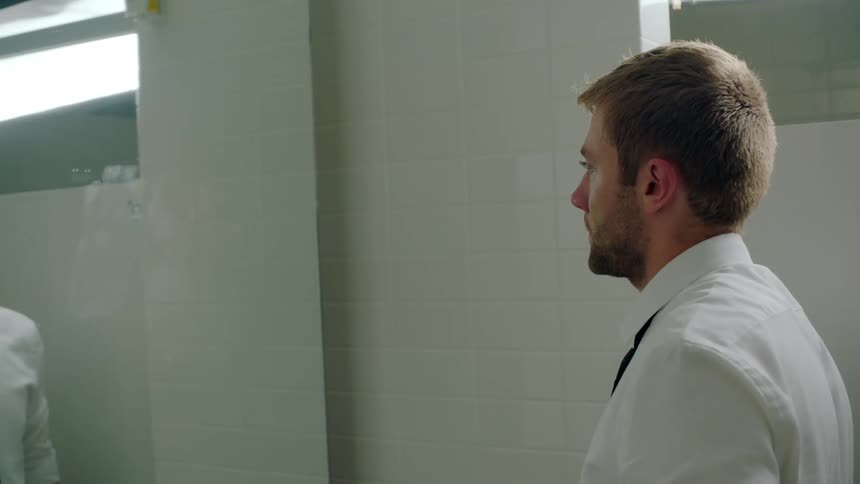A man is standing in a bathroom and looking at a mirror