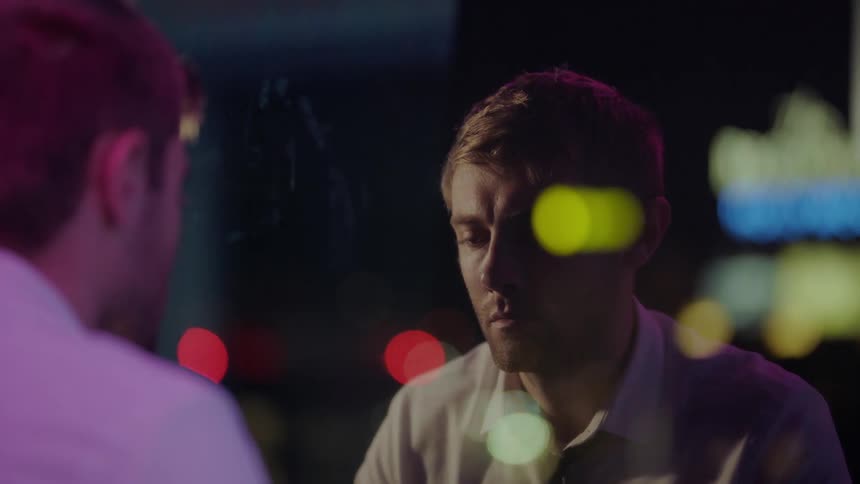A man looks off in the distance while his reflection can be seen in the glass of a window