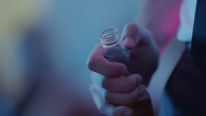 A man holds a beer bottle while nervously scratching at its label with his thumb