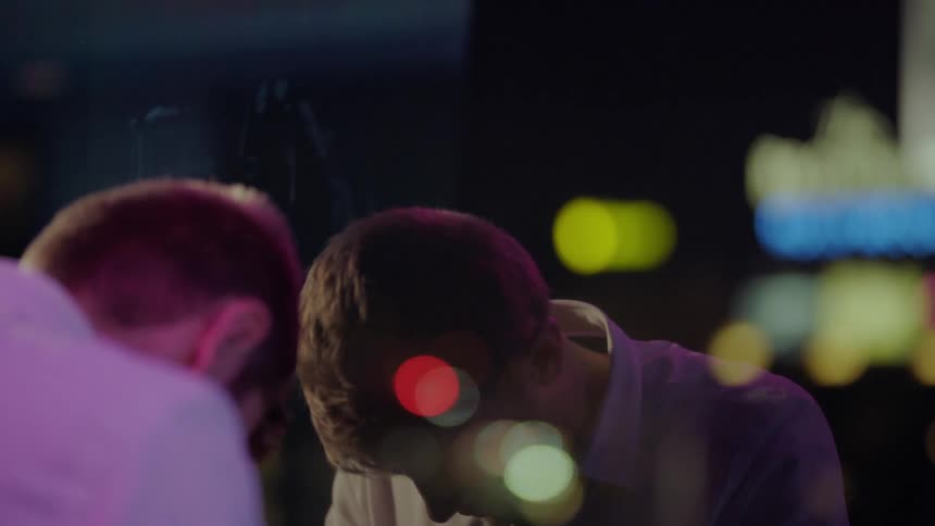 A man is in front of a mirror with colored lights nearby and he puts his head down and then walks away