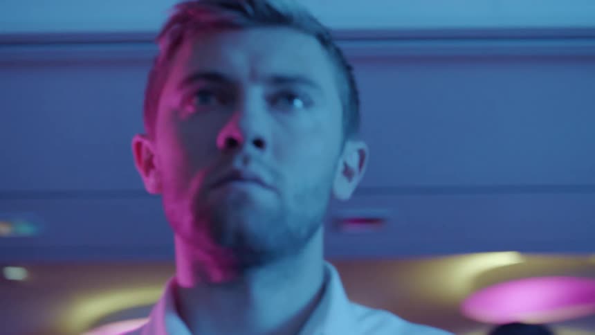 Man stands staring under colored lighting