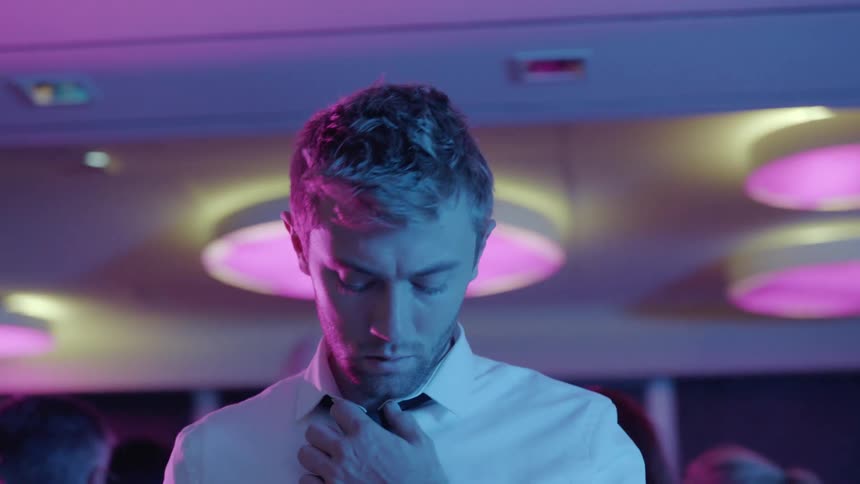 A man adjusts his necktie in the midst of a crowd of people at a party