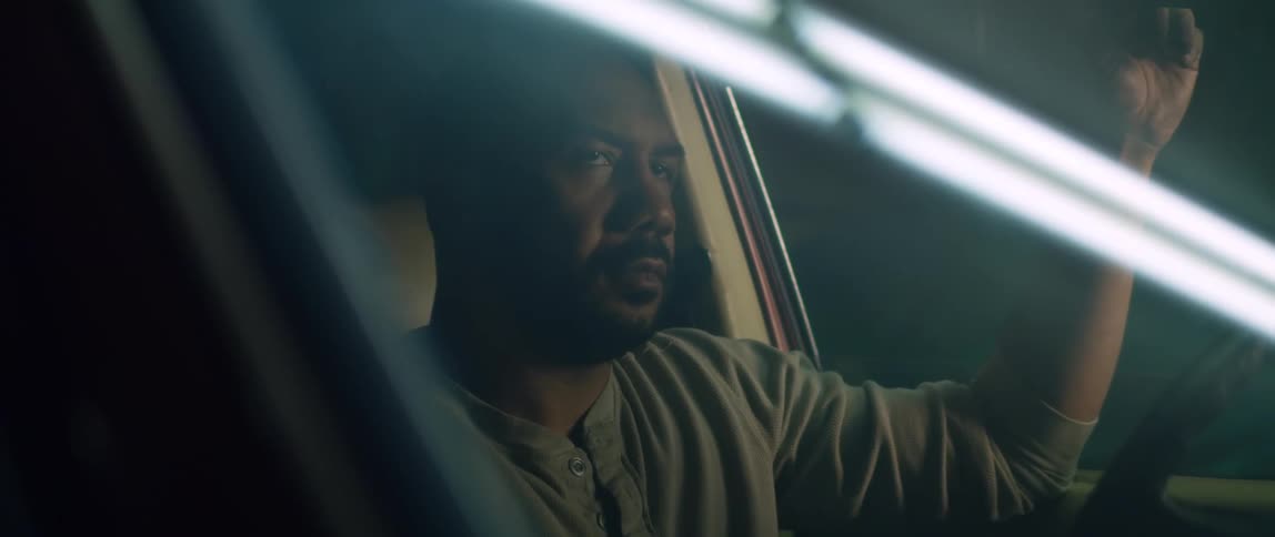 A man sits inside his car at night and looks around
