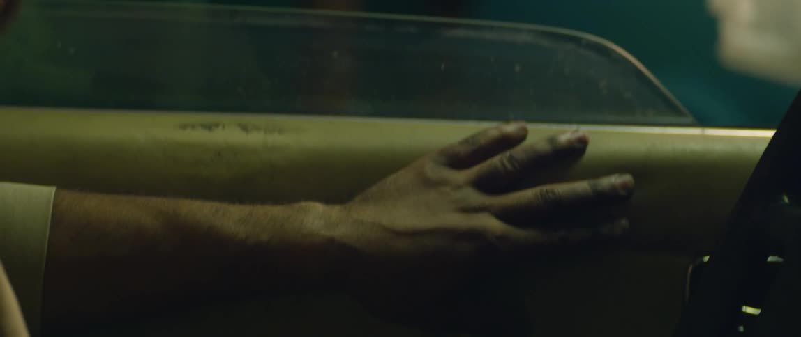 A man sits in his car at night and runs his hand over the car door and steering wheel