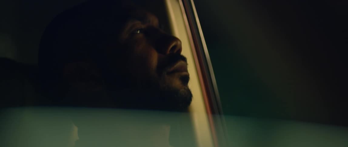 A man is sitting in the drivers seat of a parked automobile with his eyes closed and he leans his head back and opens his eyes