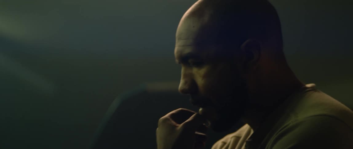 A man holds his hand to his chin as he stands and thinks in a room