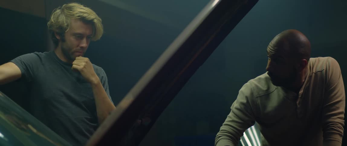 Two men chat while looking under the hood of a car