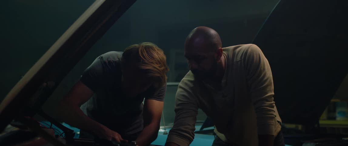 Two men work on one car before discussing a second car