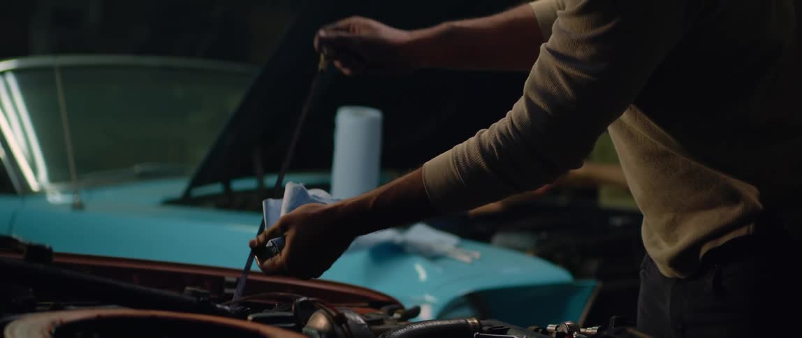 Man checks fluids in car while another man works on engine of a second car