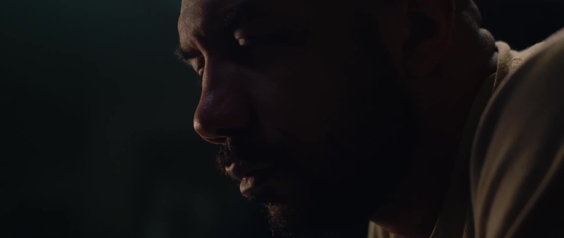 Close up of the face of a bald bearded man working inside a dimly lit garage
