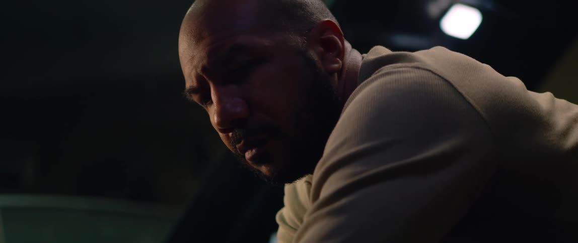 A man nervously leans on the hood of his car at night