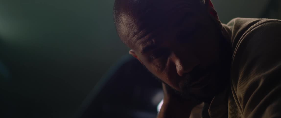 A man is in a dark room and he rubs his neck as light shines on his face from above