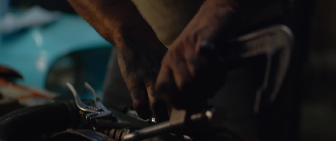 Mechanic uses a tool to repair the engine of a car inside a dimly lit garage