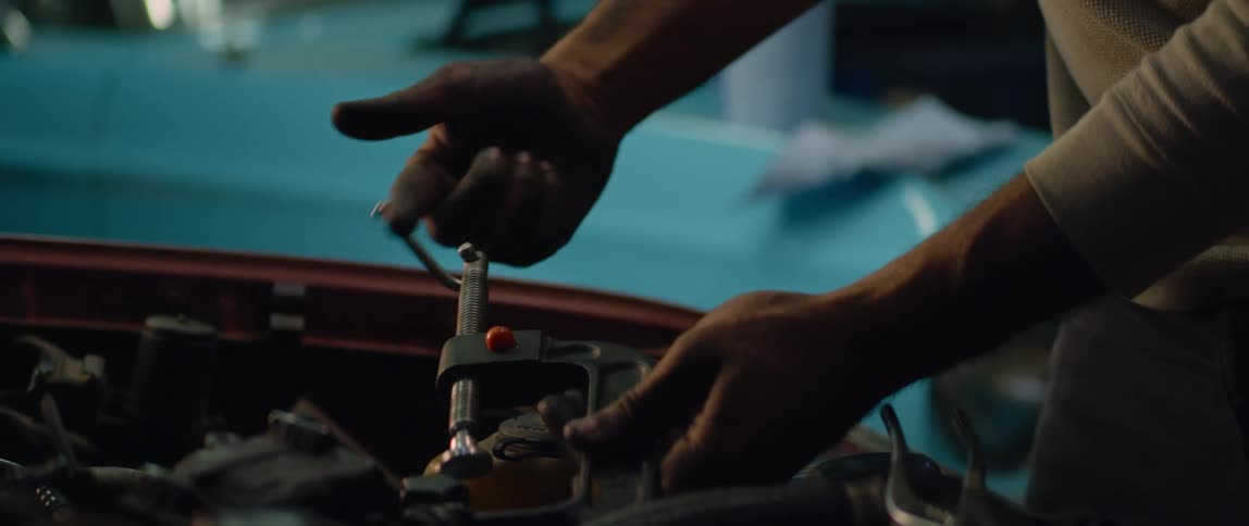 Mechanic uses a vice on a car engine inside a dimly lit garage