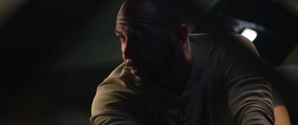 A man is in a dark room and he looks down as light shines on his face