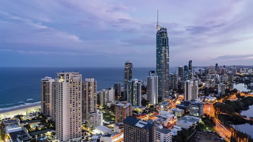 Waves roll onto the beach as day turns into night in a city